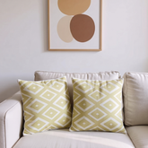 Two cream cushion covers with pale gold coloured diamond patterns on a sofa.