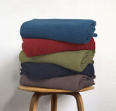 Stack of cotton thermal blankets in blue, red, green, navy and grey.