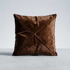 A square brown velvet throw pillow with a central crisscross pleated design, shown on a light gray studio background.