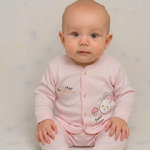 A baby sitting and wearing a light pink long-sleeve romper with a button front, featuring a bunny graphic and text on the chest, set against a soft light gray background.