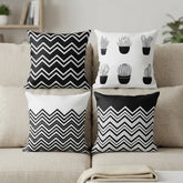 Four decorative throw pillows arranged on a beige sofa. The designs include black and white chevron patterns and black cactus illustrations on white backgrounds.