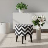 Round upholstered ottoman with a black and white chevron pattern and tapered dark legs.