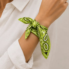 A close-up of a person's wrist wearing a bright green paisley bandana tie, styled with a white collared shirt.