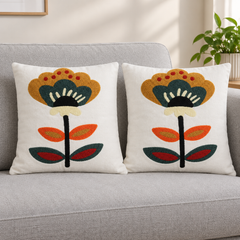 Two cream cushion covers with colourful floral embroidery on a grey sofa.