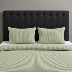 Pale green waffle-weave blanket and matching pillow covers on a bed.