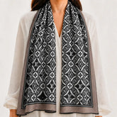 A black and white patterned scarf with Louis Vuitton monogram motifs, draped over the shoulders of a model wearing a white blouse.