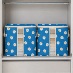 Two blue fabric storage bins with a white daisy pattern, neatly folded towels, displayed inside a white closet on a shelf.