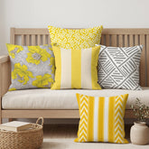 Five yellow, gray and white patterned cushion covers arranged on a wooden bench and the floor