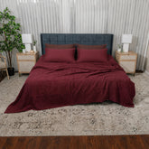 A bed dressed in a textured deep burgundy waffle blanket and matching pillow shams, styled in a modern bedroom with a blue upholstered headboard, nightstands, lamps, and a patterned rug.