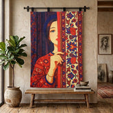 A large wall tapestry featuring a stylized illustration of a woman in a red patterned dress, hanging on a black rod in a rustic room with a wooden bench, potted plant, and framed art.