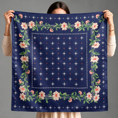 A person holds up a square navy blue scarf with a floral border and star pattern against a plain gray background.