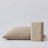 A light beige pillowcase with a matching folded sheet or pillow cover standing beside it on a clean, light gray studio background.
