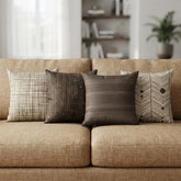 Four brown and cream cushion covers with checked, striped and chevron patterns arranged on a beige sofa.
