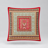 Red-bordered cushion cover with cream and green ornamental bands and a small patterned red centre.