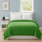 A bright green textured waffle-weave comforter set on a white bed frame in a styled bedroom with a light blue wall, white nightstand, and a window.