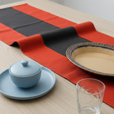 Red and black striped table runner on a wooden dining table set with plates.