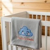 Gray baby blanket with a cloud design and text on a white crib.