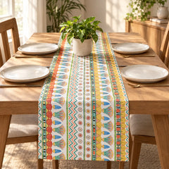 A colorful table runner with a Southwestern geometric pattern in yellow, orange, green, and blue, styled on a wooden dining table with plates and a potted plant.