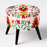 Round white ottoman with colourful floral upholstery and dark tapered legs.