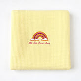 Folded pale yellow waffle-weave baby blanket with a rainbow motif.