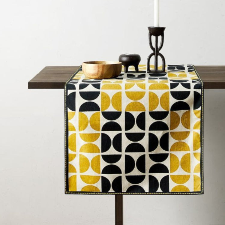 Black, white and mustard geometric table runner beneath candleholders.