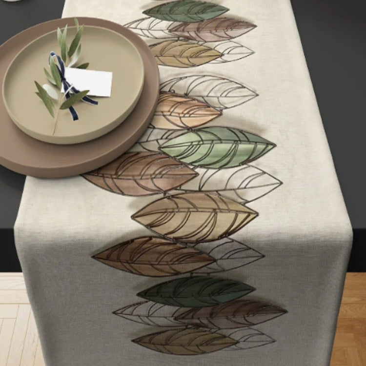 Cream table runner with outlined autumn leaves in muted green and brown.