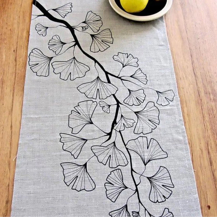 Close-up of outlined ginkgo-like leaves on a light grey table runner.