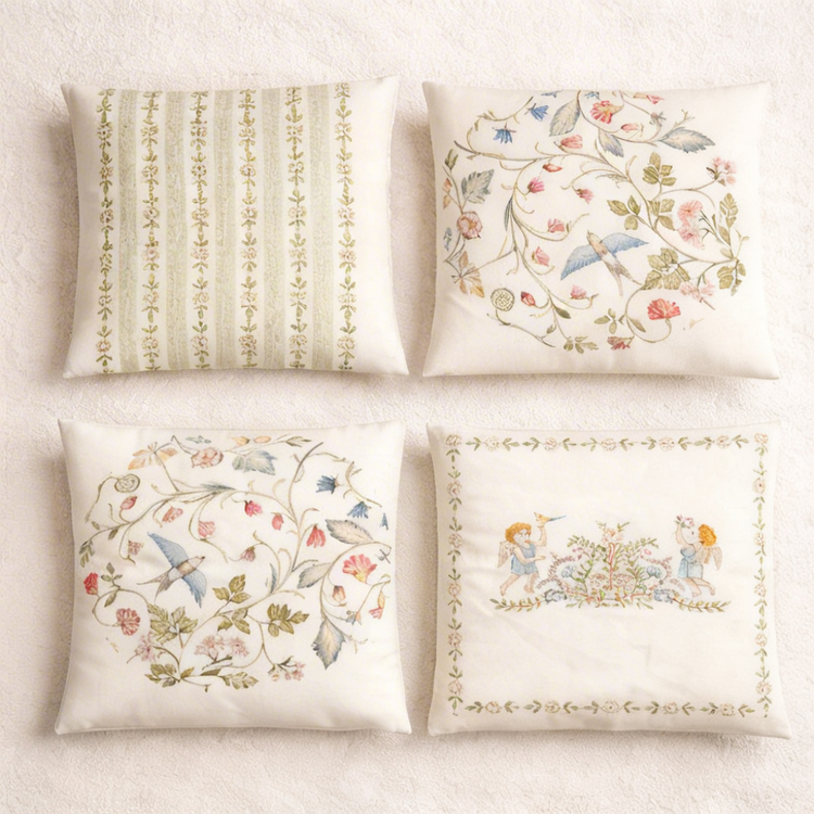 Four cream cushion covers with subtle green stripes and delicate floral and bird illustrations.