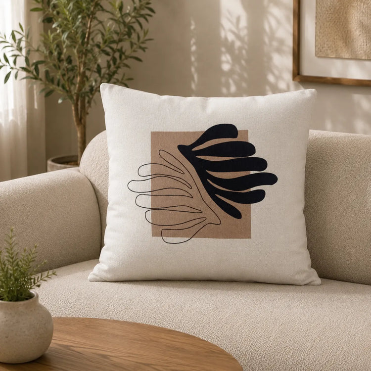 Cream filled cushion with a black abstract leaf over a beige square and fine curved lines.