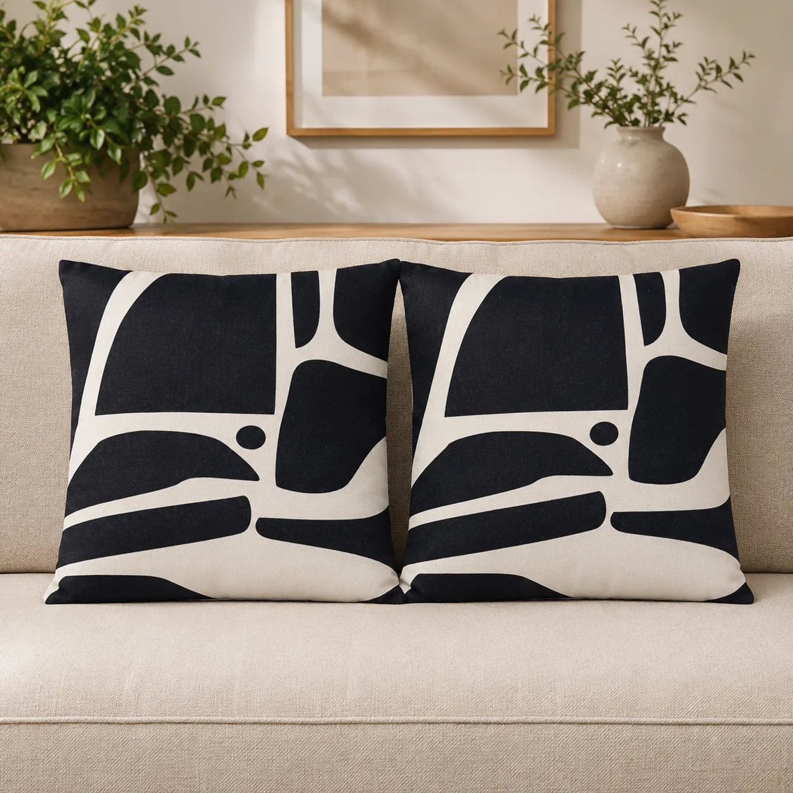 Two cream cushion covers with broad black abstract curved shapes on a sofa.