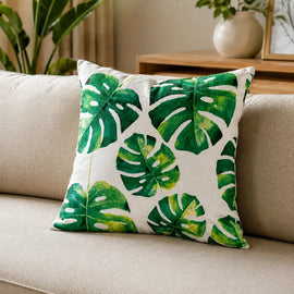 White filled cushion with large green monstera leaves.