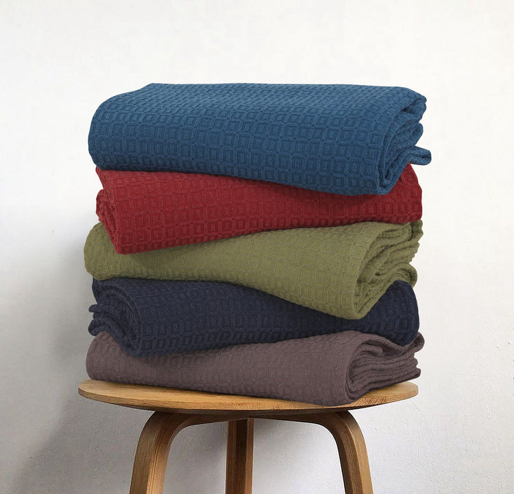 Stack of cotton thermal blankets in blue, red, green, navy and grey.