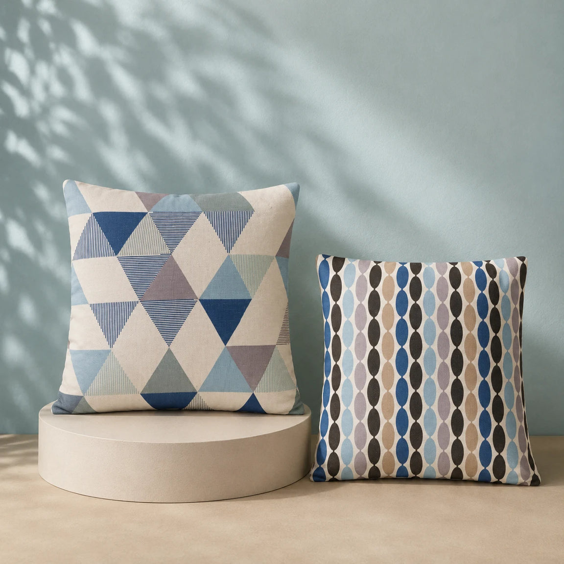 Two cushion covers with blue and cream triangle and leaf-like geometric patterns.