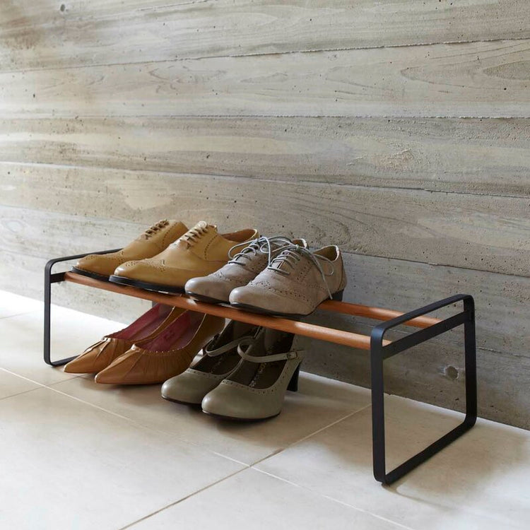 Low black shoe rack with wood-tone rails holding shoes