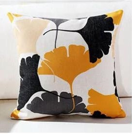 White cushion cover with large black, grey and yellow fan-shaped leaves.