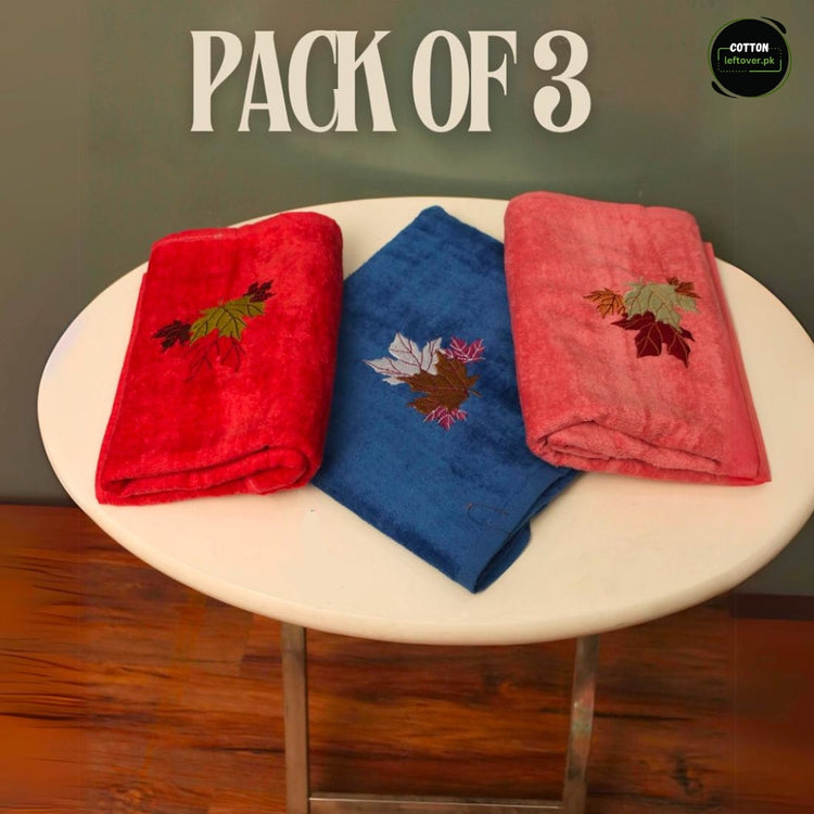 Three colourful towels in red, blue and pink with small decorative embroidered motifs.