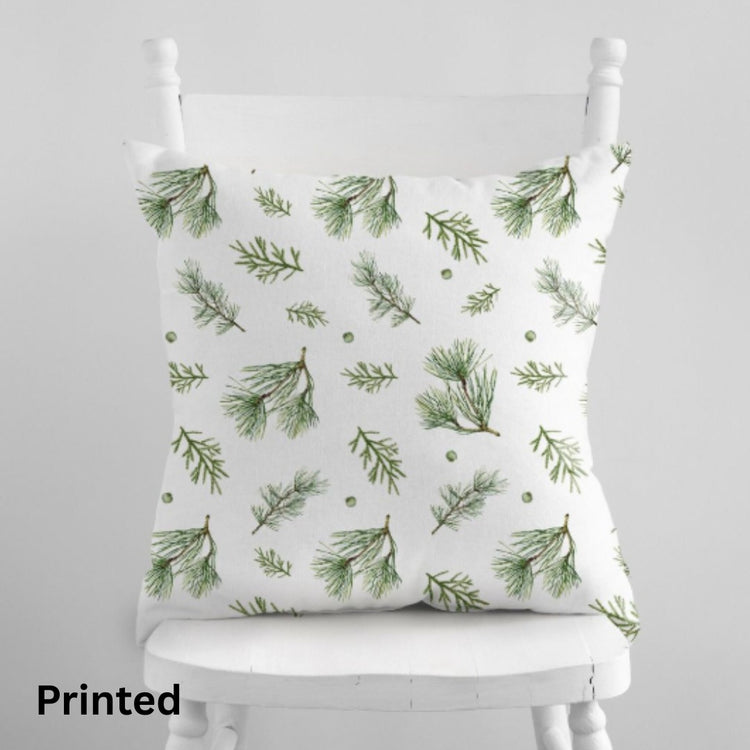 White cushion cover with scattered green botanical sprigs on a wooden chair.