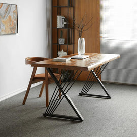 Brown-top desk with black crossed leg supports and narrow diagonal rods beside a wooden chair.
