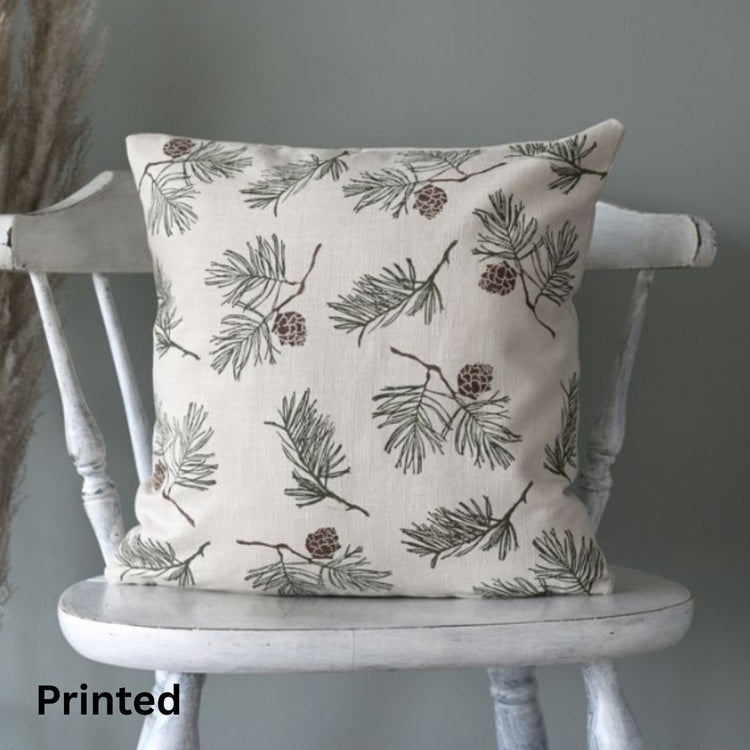 Cream cushion cover with fine grey-green leaves and small flowers on a wooden chair.