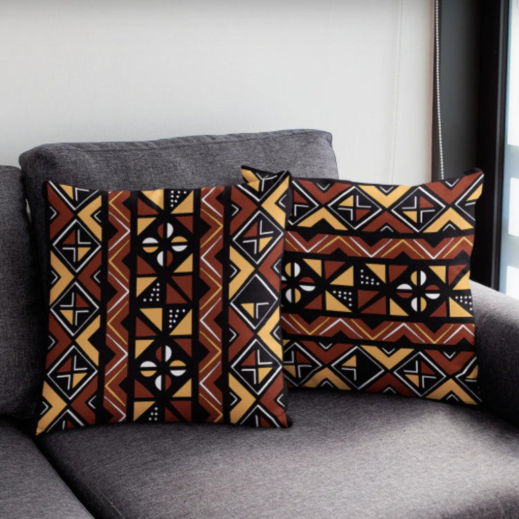 Two dark cushion covers with orange, cream and brown geometric bands on a grey chair.