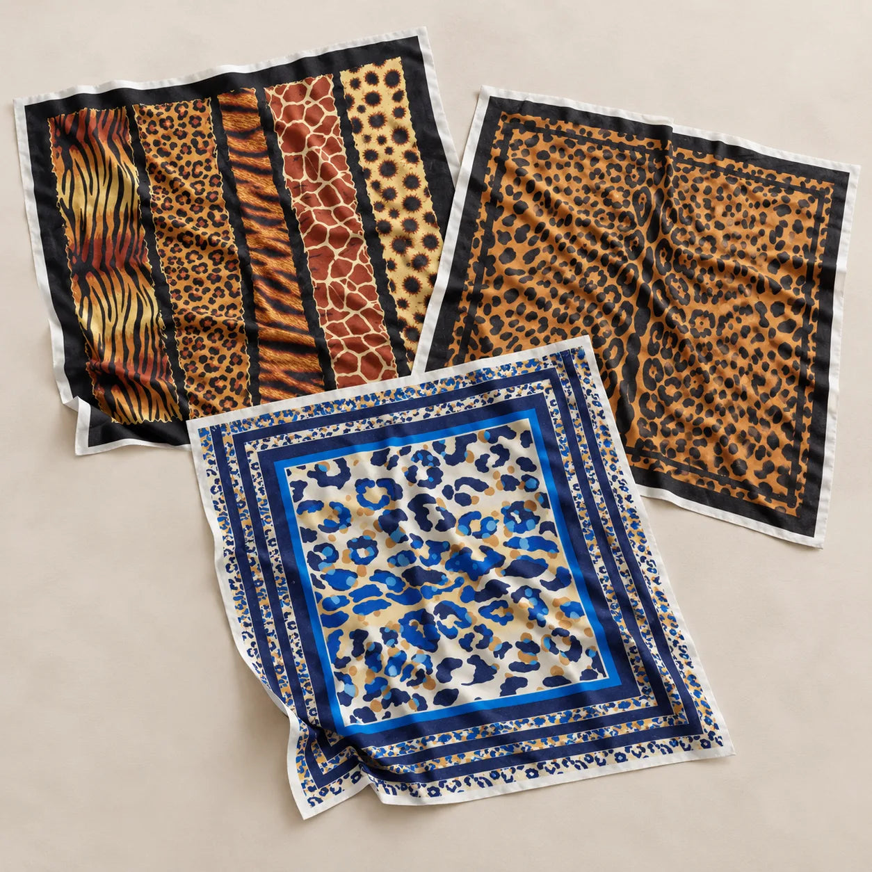 Three square patterned scarves laid flat on a light beige background. One scarf features vertical stripes with tiger, leopard, and giraffe prints in orange, brown, and black.