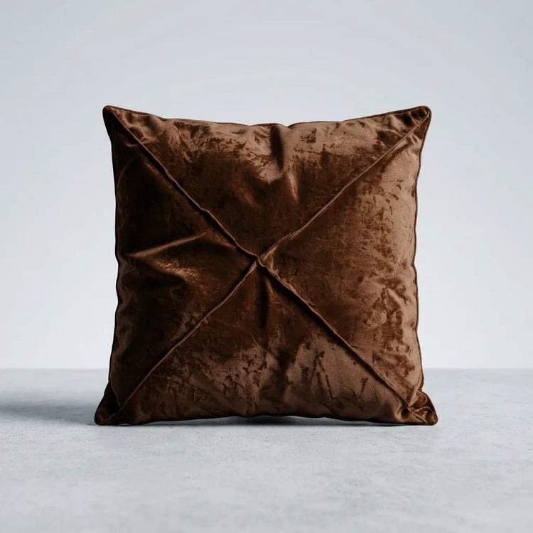 A square brown velvet throw pillow with a central crisscross pleated design, shown on a light gray studio background.