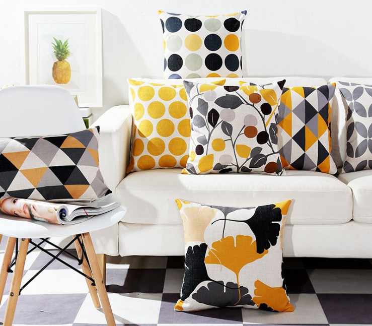 Yellow and grey patterned cushion covers arranged on a white sofa and chair.