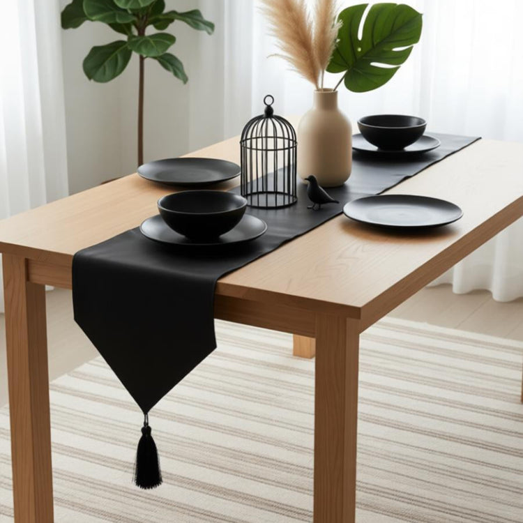 Black table runner with a pointed tasselled end beneath black crockery.