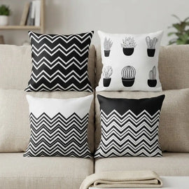 Four decorative throw pillows arranged on a beige sofa. The designs include black and white chevron patterns and black cactus illustrations on white backgrounds.