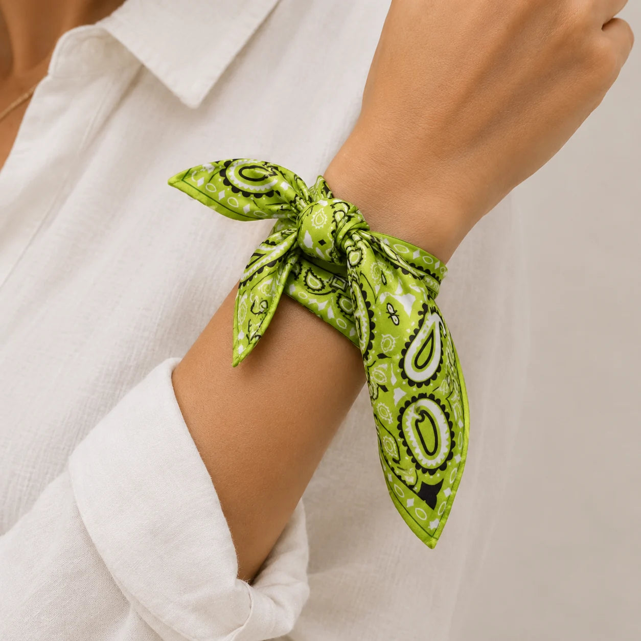 A close-up of a person's wrist wearing a bright green paisley bandana tie, styled with a white collared shirt.