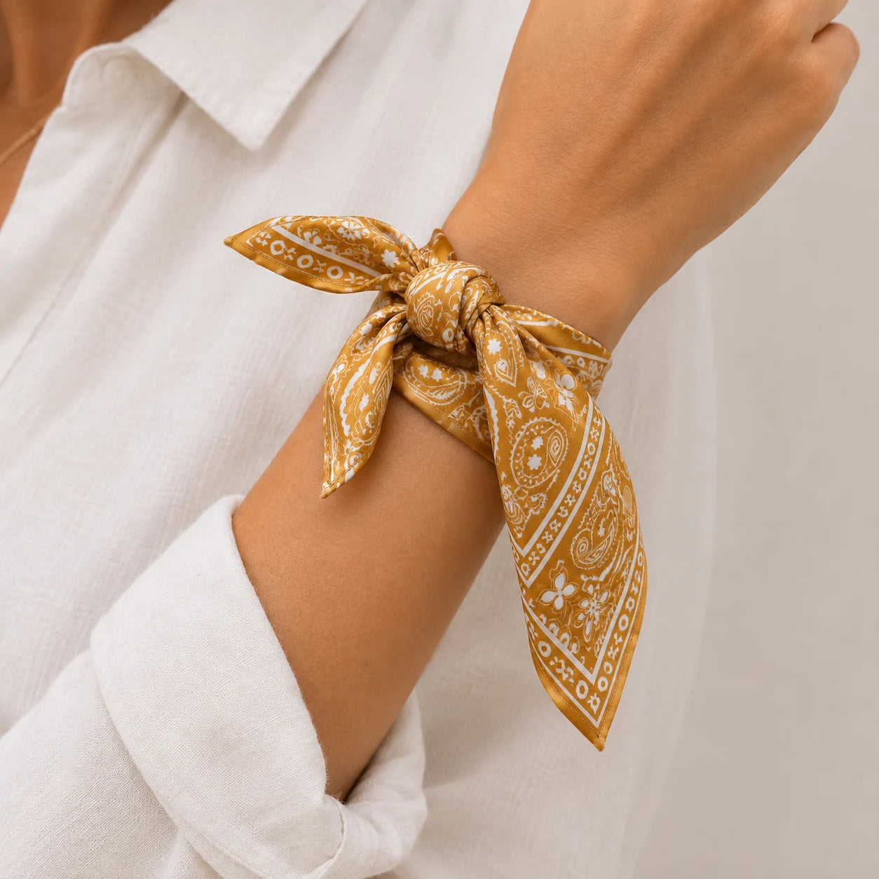 A close-up of a person's wrist wearing a bright paisley bandana tie, styled with a white collared shirt.
