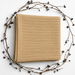 Folded camel-colored baby blanket with a fine striped texture, surrounded by decorative berry branches.