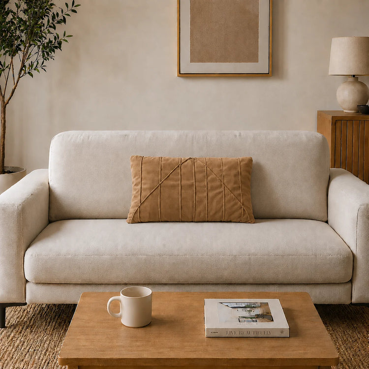 Rectangular tan filled cushion with angular stitched lines on a cream sofa.