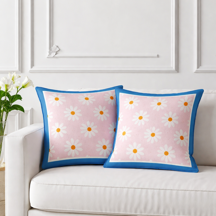 Two peach cushion covers with small white daisies and blue borders on a sofa.